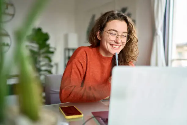young-happy-woman-student-using-laptop-watching-webinar-writing-at-home
